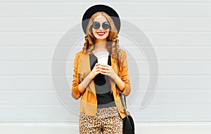 Elegant woman with coffee cup wearing retro elegant hat, sunglasses, brown jacket