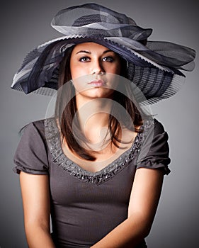 Elegant Woman Face Portrait hidden by Black Hat. Beauty Fashion Model with Red Lips and Eye Make up over dark Gray