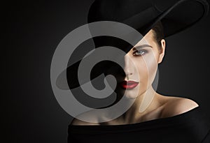 Elegant Woman Face Portrait hidden by Black Hat. Beauty Fashion Model with Red Lips and Eye Make up over dark Gray Background