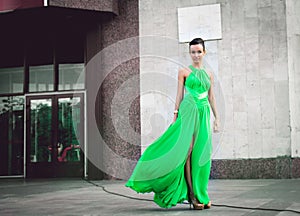 Elegant woman in green dress posing against a concrete wall