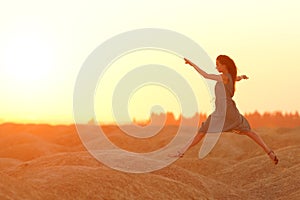 Elegant woman in long dress with straw hat junping elegant on sandy hills in desert. Sunrise, backlight photo