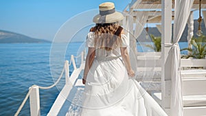 Elegant woman in long dress walking on the wooden sea pier and seating in gazebo enjoying view of the beach and ocean