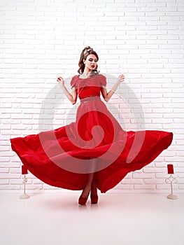 elegant woman in a long flittering red dress is standing in a white room photo