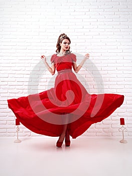 elegant woman in a long flittering red dress is standing in a white room