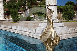 Elegant woman in long golden evening dress is posing outdoor in luxury resort in Turkey. Female model in amazing long dress. Vogue