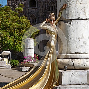 Elegant woman in long golden evening dress is posing outdoor in luxury resort in Turkey. Female model in amazing long dress. Vogue