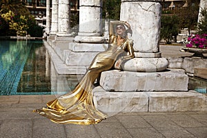 Elegant woman in long golden evening dress is posing outdoor in luxury resort in Turkey. Female model in amazing long dress. Vogue