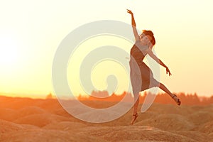 Elegant woman with long hair in long dress dancing elegant on sand in desert. Sunrise, backlight photo