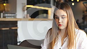 Elegant woman with modern laptop . Young lady with serious face expression works at computer in cafe and looking with