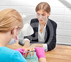 Elegant woman in office suit sitting and receiving manicure in beauty salon.