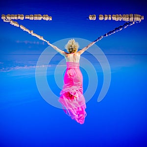 Elegant woman in pink dress suspended in surreal blue sky