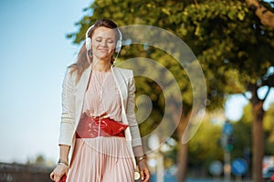 elegant woman in pink dress and white jacket in city walking
