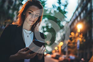 Elegant woman pointing on screen smartphone background lights in night city street, tourist girl using internet technology calls