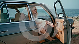 Elegant woman posing auto with open door. Girl sitting in retro car at sea shore