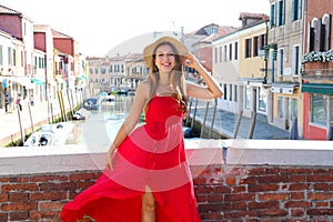 Elegant woman in red long dress walking on bridge in the old town of Murano, Venice, Italy