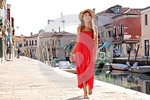 Elegant woman in red long dress walking in the old town of Murano, Venice, Italy