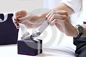 Elegant woman`s hands unleash a bow on a gift box. The concept of a holiday, congratulations and love.