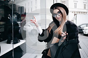 Elegant woman with shopping bags is standing near a shop window with clothes. Girl is engaged in shopping at leisure