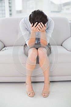 Elegant woman sitting with head in hands on sofa