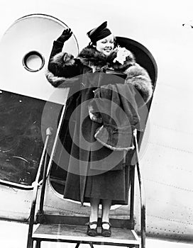 Elegant woman stepping out of an airplane and waving