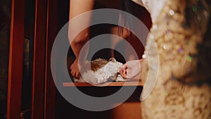 Elegant woman in a strapless dress holding a lace gown, contemplating it thoughtfully in a warmly lit room