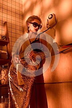 elegant woman in sunglasses holding retro telephone in kitchen