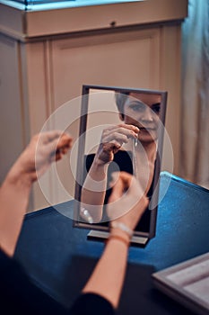 Elegant woman is trying on new jewel necklace in front of the mirror