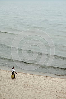 Elegant woman walking along sea with shoes and bag in hands