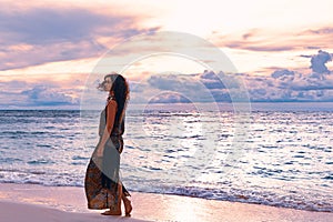 Elegant woman walking by the shore line at the beach. Sunset and silhouette