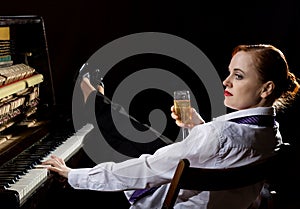 Elegant woman in a white shirt and tie sitting next to the piano and drinks champagne photo