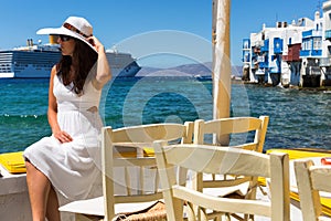 Elegant woman in white sits at the waterfront of Little Venice in Mykonos, Greece