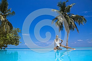 Elegant woman in white swimsuit in pool on tropical Maldives island. Beautiful bikini body girl in pool with view on horizon.