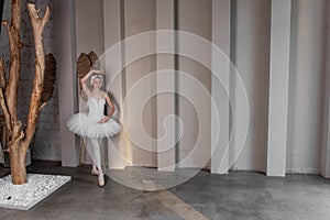 Elegant young ballerina performs beside large windows, poised stance, delicate white tutu