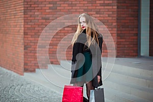 Elegant young beautiful women holding shopping bags, standing on shop stairs. Sale, consumerism and people concept