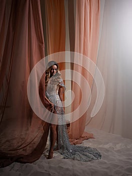 An elegant young blonde in a luxurious dress behind a curtain