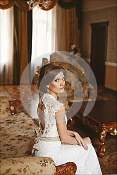 Elegant young bride with beautiful blue eyes and with wedding hairstyle in the stylish dress with lace sits on the