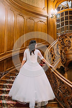 Elegant young bride at old vintage palace walking up big wooden stairs