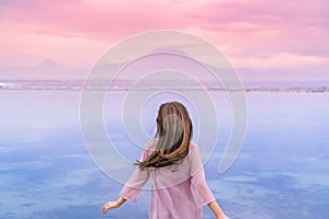 A elegant young brunette girl blown by the wind running towards the ocean and mountains. The girl stands with her back