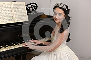 Elegant young brunette with oriental appearance in a white dress at the piano