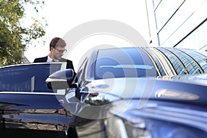 Elegant young businessman entering his comfortable car while standing outdoors