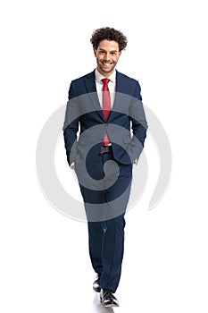 Elegant young businessman in navy blue suit walking with hands in pockets