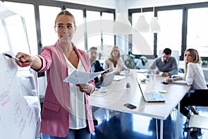 Elegant young businesswoman pointing at white blackboard and explain a project to her colleagues on coworking place