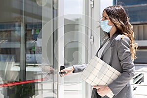 Elegant young Caucasian businesswoman entering her workplace. She is wearing a medical mask to prevent the spread of the Covid-19