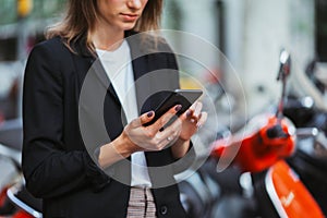 An elegant young girl in a business suit uses mobile app in her smartphone to remotely activate and pre pay for a street scooter