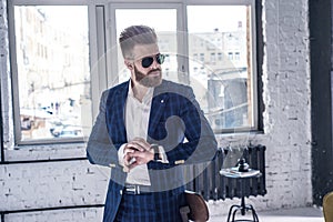 Elegant young handsome man with beard wearing glasses and watchers. Loft studio fashion portrait