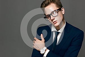 Elegant young handsome man with a wristwatch and glass glasses. Fashion portrait studio