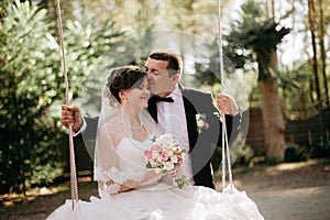 Elegant young happy wedding couple is sitting at green grass on