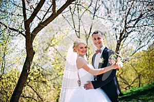 Elegant young happy wedding couple is sitting at green grass on