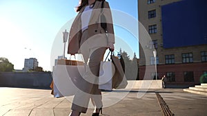 Elegant young lady holds shopping bags going at city square after purchases. Attractive woman carries paper packets