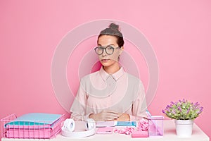 Elegant young lady at working desk, wearing glasses and pastel tone pink shirt, load with the work at the desk, isolated